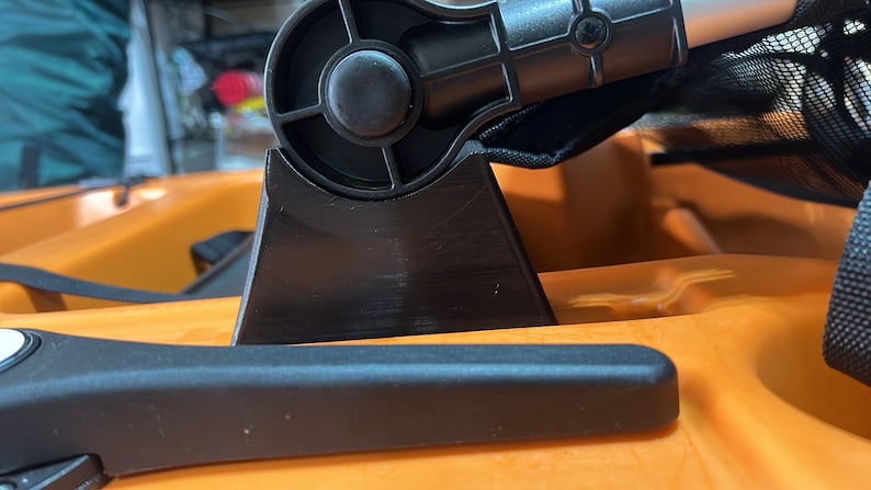 Pu&ograve; includere: Primo piano di un attacco per sedile da kayak nero con una manopola girevole. L'attacco &egrave; montato su un kayak arancione brillante.