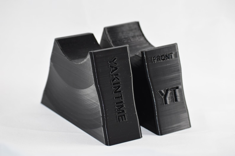 Pu&ograve; includere: Due oggetti neri stampati in 3D, uno con il testo "YAKINTIME" e l'altro con il testo "FRONT YT".