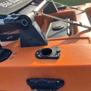 Pu&ograve; includere: Primo piano di un kayak arancione brillante con accenti neri. Il kayak ha un sedile nero con il testo "Old Town" e "Sportsman" stampato su di esso. Il kayak ha un portacanne nero, una cinghia nera e una maniglia nera.