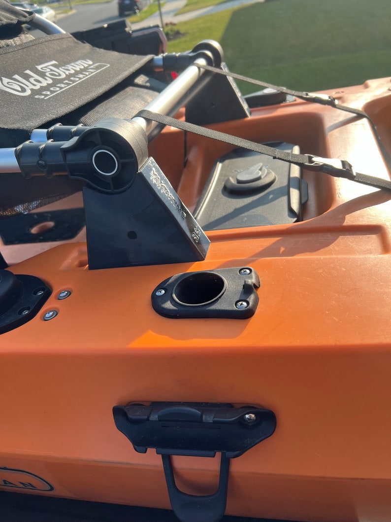 Pu&ograve; includere: Primo piano di un kayak arancione brillante con accenti neri. Il kayak ha un sedile nero con il testo "Old Town" e "Sportsman" stampato su di esso. Il kayak ha un portacanne nero, una cinghia nera e una maniglia nera.