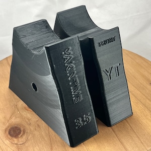 Pu&ograve; includere: Due blocchi di plastica nera a forma di cuneo con il testo "WAKE'N TIME 3.5" e "YT FRONT" stampato su di essi. I blocchi sono su una superficie di legno.