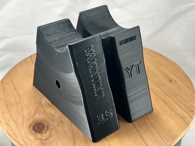 Pu&ograve; includere: Due blocchi di plastica nera a forma di cuneo con il testo "WAKE'N TIME 3.5" e "YT FRONT" stampato su di essi. I blocchi sono su una superficie di legno.