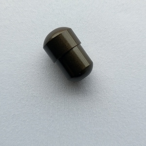 Puede incluir: Un pequeño contenedor de forma de cápsula de color marrón oscuro metálico.