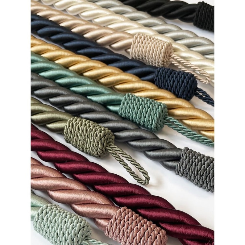 May include: A collection of twisted rope cords in various colors, including gold, green, burgundy, and gray. The cords are made of a soft, silky material and have a tassel at the end.