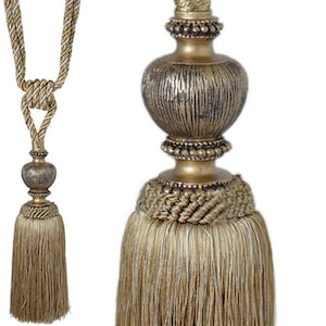 May include: Gold tassel tieback with a decorative, textured, round finial. The tassel is made of a woven cord and has a fringe.