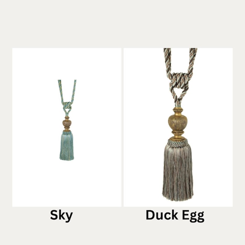 May include: Two decorative curtain tiebacks with tassels. The tieback on the left is sky blue with a gold bead. The tieback on the right is a light grey with a gold bead.