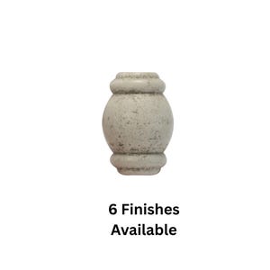 Puede incluir: Un pomo decorativo de madera gris claro con un acabado moteado. El pomo tiene una forma redondeada de reloj de arena con una parte superior e inferior cilíndricas. El texto en la parte inferior dice "6 Acabados Disponibles."