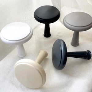 May include: Five different colored ceramic curtain tiebacks in the shape of a mushroom. The tiebacks are in white, cream, gray, black, and light gray.