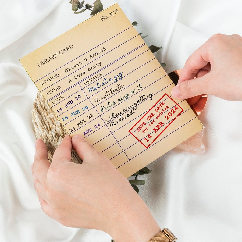 May include: A library card-style wedding announcement with the title "A Love Story" and details of a couple's relationship. The card is stamped with "SAVE THE DATE" for 14 April 2024, held by hands.