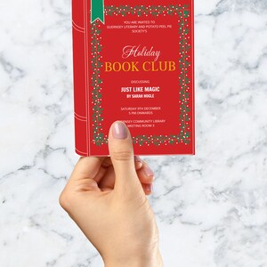 Op de afbeelding: Een rode uitnodigingskaart voor een Holiday Book Club, vastgehouden door een hand. De kaart bevat tekst, waaronder "Holiday Book Club" en "Just Like Magic by Sarah Hogle". Het ontwerp bevat groene en witte decoratieve elementen, met een groen bladwijzer.