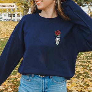 a woman wearing a blue sweatshirt with a rose embroidered on it