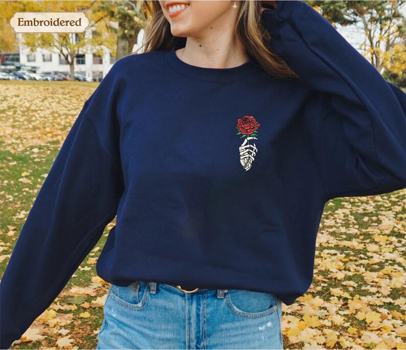 a woman wearing a blue sweatshirt with a rose embroidered on it
