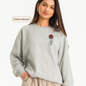 a woman wearing a grey sweatshirt with a rose embroidered on it