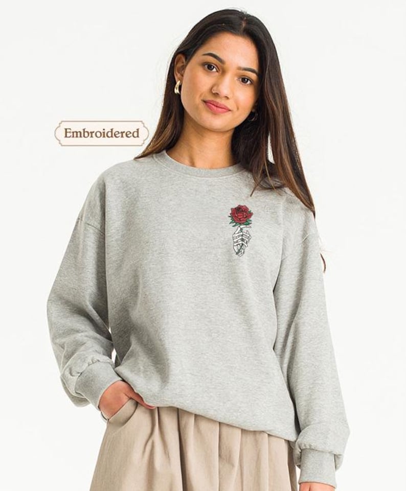 a woman wearing a grey sweatshirt with a rose embroidered on it