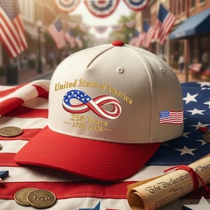 May include: A cream and red baseball cap with the words "United States of America" and an infinity symbol in the colours of the American flag. The cap commemorates 250 years, 1776-2026, and has a small American flag patch.