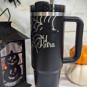 A black 30oz Stanley Quencher Tumbler engraved with a beautiful spider web across the top of the cup with the name Keira across it. The spider web engraving and name dynamically meshes with the Stanley Logo embedded in the tumbler.