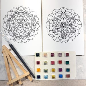 May include: A watercolor painting kit featuring two mandala designs, a small wooden easel, a paintbrush, and a palette of 20 watercolor paints in various colors. The mandala designs are black line drawings on white paper.