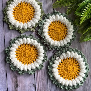 Könnte beinhalten: Vier gehäkelte Untersetzer in einem Gänseblümchen-Design. Die Untersetzer sind aus gelbem, weißem und grünem Garn gefertigt.