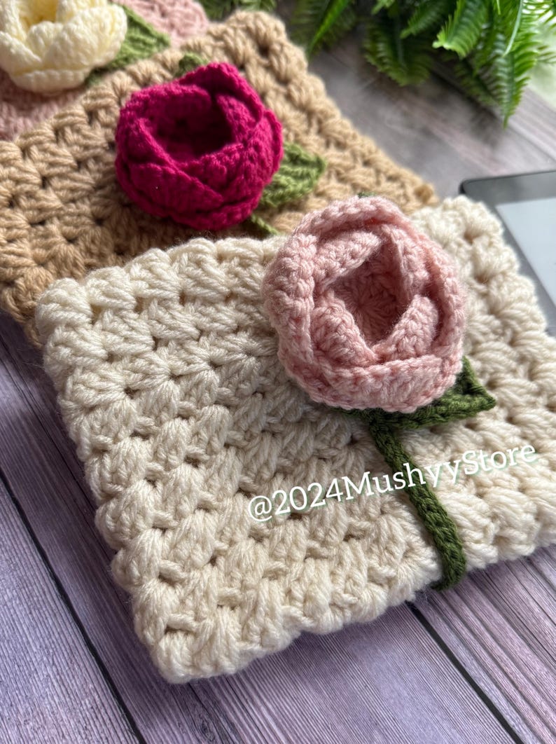 May include: Three crocheted flower embellishments in beige, pink, and red. The flowers are attached to a beige crocheted fabric with green stems.
