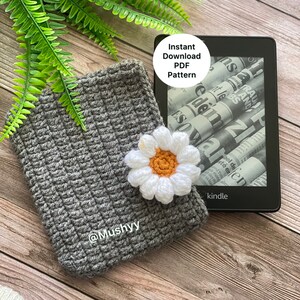 May include: A gray crocheted Kindle cover with a white daisy flower appliqu&eacute;. The cover has the text "@Mushyy" embroidered on it. The image includes the text "Instant Download PDF Pattern".