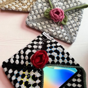 May include: Crocheted envelope-style cases in beige, gray, and black with white accents. Each case features a crocheted rose in pink or red, with green leaves. One case holds a tablet.