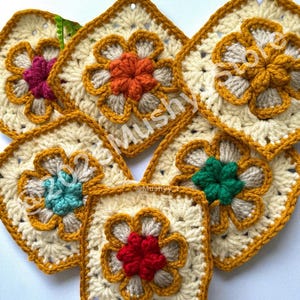 May include: A collection of handmade crochet squares with a floral design. Each square features a cream-colored base, a flower in the center with various colors, and a mustard yellow border. The squares are arranged together.