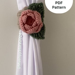 May include: A crocheted flower curtain tieback in shades of pink, beige, and green. The tieback is attached to a white curtain. The text "Instant Download PDF Pattern" is visible in the image.