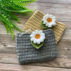 May include: Two crocheted pouches with daisy flower embellishments. The pouch on the left is gray and the pouch on the right is beige.