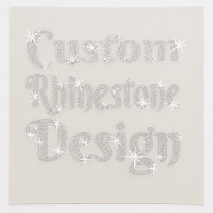 May include: A square graphic featuring the text Custom Rhinestone Design written in three lines. The letters are composed of small, silver-coloured, reflective rhinestones that create a sparkling effect against a plain, light-coloured background.