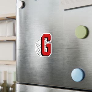 May include: A red letter G with a white basketball behind it. The letter G is in a varsity style font.