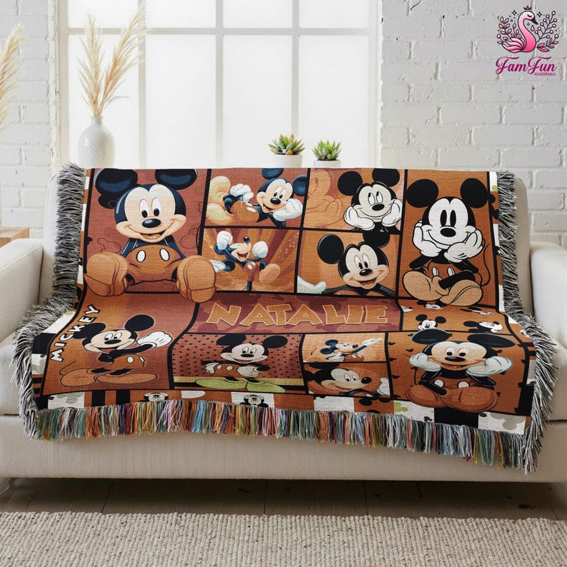 A Mickey Mouse-themed throw blanket with the name Natalie printed on it, placed on a white couch.