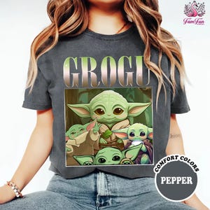 A person wearing a gray t-shirt with a graphic design featuring a group of baby alien characters, specifically the character Groot, along with the text "Comfort Colors Pepper".