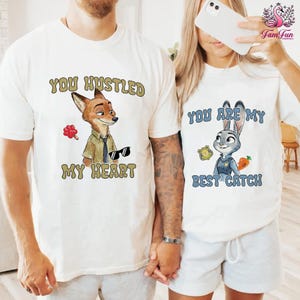 A man and a woman wearing matching white t-shirts with cartoon animal characters and text printed on them.