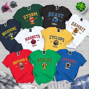 May include: Nine different t-shirts featuring X-Men characters. Each shirt has a different character, including Wolverine, Storm, Beast, Gambit, Magneto, Cyclops, Professor X, Rogue, and Jean Grey. The shirts are all white, black, green, blue, red, and yellow. Each shirt has the character's name and the year they were established.