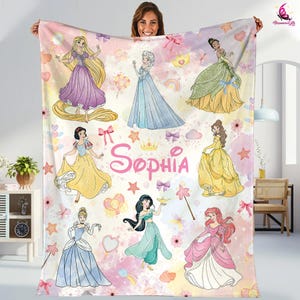 May include: A pink and white fleece blanket with a watercolor background featuring Disney princesses. The blanket has a pink and white floral pattern with stars and bows. The princesses include Cinderella, Snow White, Ariel, Jasmine, Rapunzel, Belle, Elsa, and Aurora. The blanket is personalized with the name "Sophia".