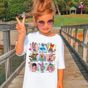 A young girl wearing a white t-shirt with cartoon animal characters and making a peace sign gesture.