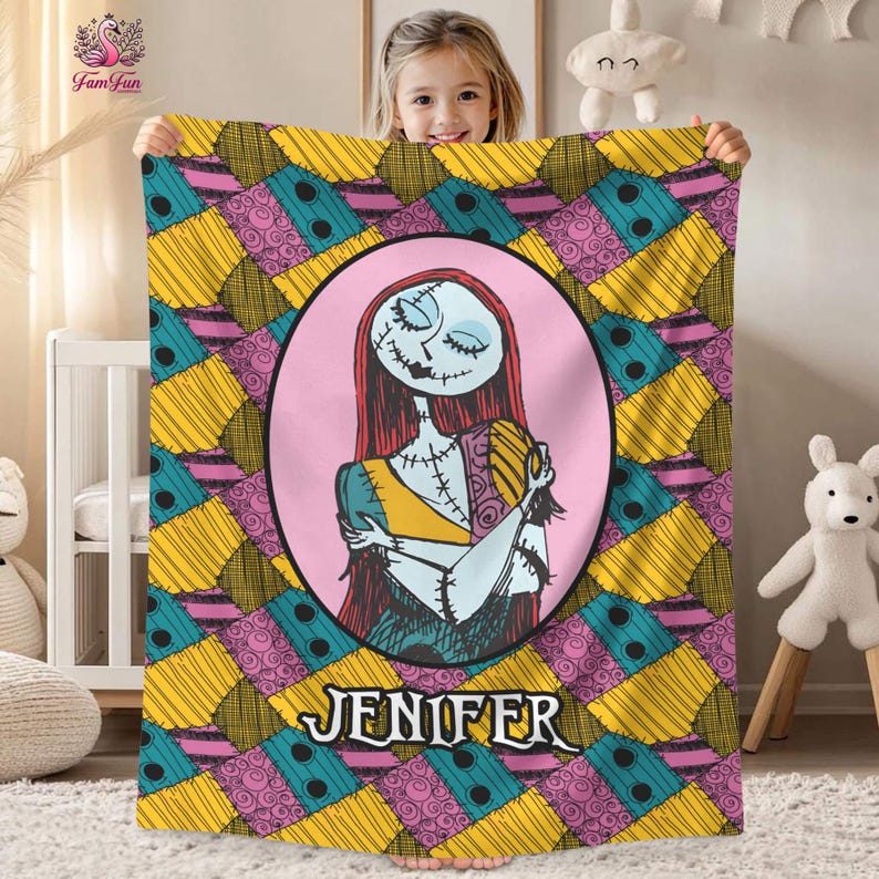 May include: A colorful blanket featuring a patchwork design in yellow, teal, pink, and black. The center of the blanket has a pink oval with a cartoon character illustration and the name "JENIFER" in a stylized font. The blanket is held by a child.
