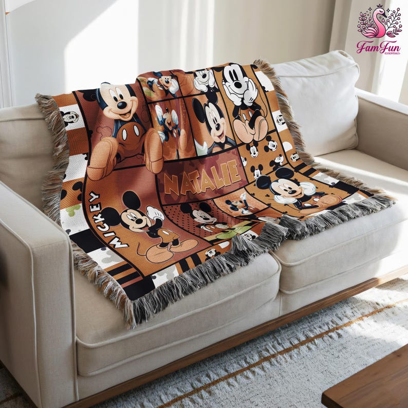 a comfy couch with a large, colorful throw blanket on it. The blanket is decorated with various cartoon characters, including Mickey Mouse and Donald Duck. The blanket is placed on a white couch, and there is a wooden coffee table in front of it.