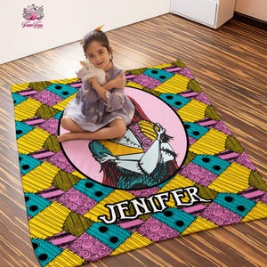 May include: A colorful rug featuring a cartoon character in a pink circle, with the name "JENIFER" in white. The rug has a patchwork design in yellow, teal, and pink. A young person is sitting on the rug.