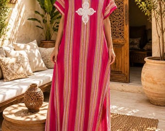 May include: A floor-length kaftan dress in vibrant magenta with vertical stripes in shades of pink, orange, and white. The garment features short sleeves, a notched neckline, and a prominent white embroidered floral motif on the chest.