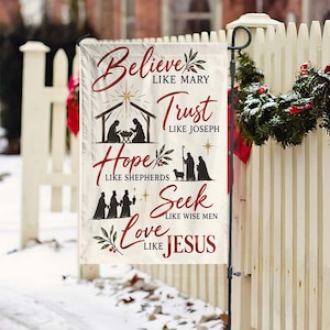 May include: A rectangular garden flag with a cream background and red text featuring a nativity scene. The text reads: Believe like Mary, Trust like Joseph, Hope like Shepherds, Seek like Wise Men, Love like Jesus, with black silhouettes.