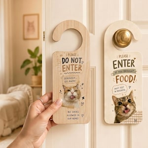 Op de afbeelding: Twee houten deurhangers met kattenontwerpen. Eén leest "DO NOT ENTER" met een kattenafbeelding en "NO SHOES ALLOWED". De andere zegt "ENTER IF YOU BROUGHT FOOD!" met een kattenafbeelding. Beide hebben een gebogen bovenkant.