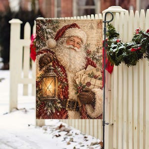 May include: A rectangular garden flag featuring a vintage-style illustration of Santa Claus with a white beard, wearing a red coat with white fur trim. He holds a lit lantern in one hand and a stack of letters in the other, set against a background of script text.