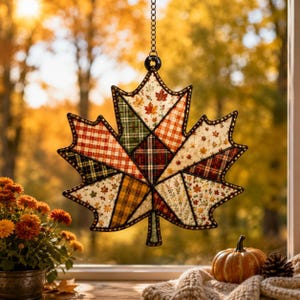 Peut inclure: Une d&eacute;coration suspendue en forme de feuille d'&eacute;rable compos&eacute;e d'un assemblage de tissus aux motifs automnaux, incluant des carreaux, du vichy et des imprim&eacute;s de petites feuilles, le tout encadr&eacute; de m&eacute;tal sombre et suspendu par une cha&icirc;ne argent&eacute;e.