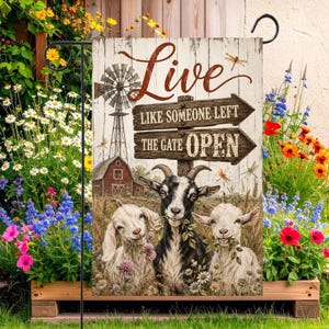 May include: A rectangular garden flag featuring a rustic wooden background with a windmill and barn illustration. The text reads Live Like Someone Left The Gate Open. Three goats are depicted in the foreground amidst wildflowers and dragonflies.