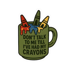 Może przedstawiać: Zielona naklejka z kubkiem z trzema kredkami i napisem "DON'T TALK TO ME TILL I'VE HAD MY CRAYONS". Kredki są czerwone, zielone i żółte, z roztopionym woskiem spływającym po boku kubka.