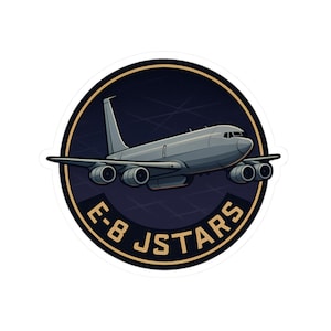 May include: A sticker featuring a gray airplane with four engines, set against a dark blue background with a grid pattern. The text "E-8 JSTARS" is in gold lettering, encircling the plane within a gold-bordered circle. The sticker has a white border.