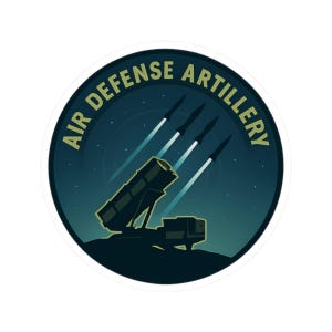 May include: A round sticker with the text "AIR DEFENSE ARTILLERY" in a circular design. The sticker features a dark blue background with a silhouette of a missile launcher and four missiles ascending into the night sky.