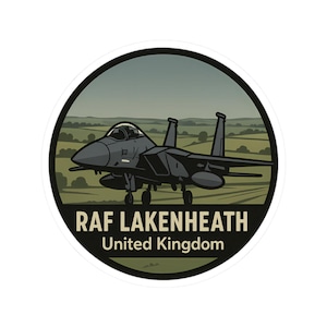 May include: A circular sticker featuring a gray fighter jet in front of a green and brown landscape. The text "RAF LAKENHEATH United Kingdom" is displayed in white letters on a black banner at the bottom of the sticker.