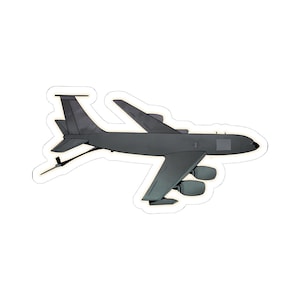 May include: A gray military aircraft with a long, narrow fuselage and a single tail fin. The aircraft has four engines and a large, rectangular window on the side.
